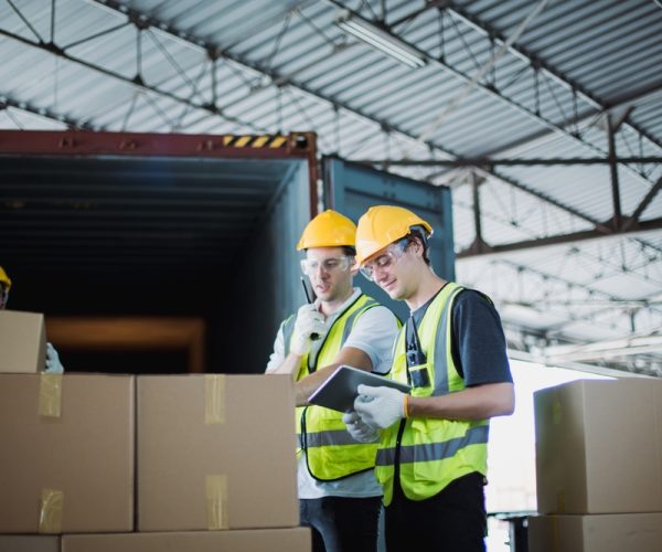 Logistics,Workers,In,Safety,Vests,And,Helmets,Loading,Packages,From